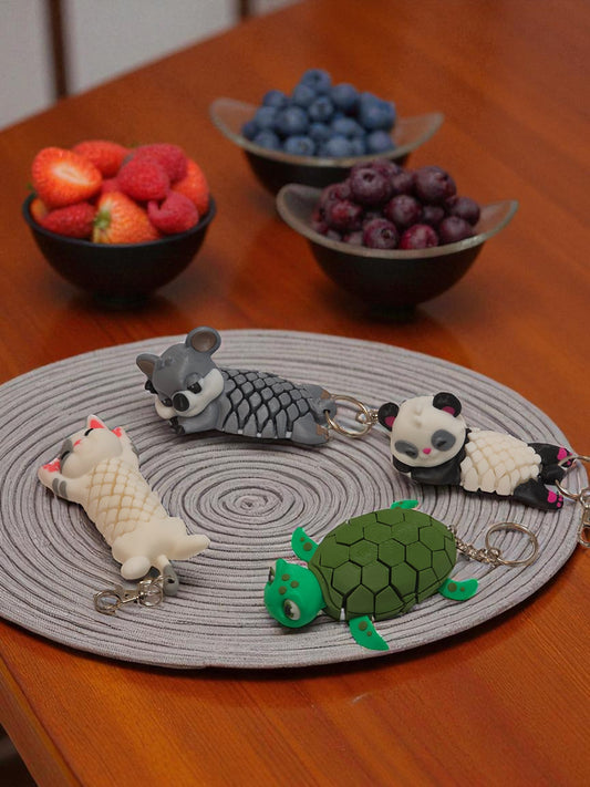Keychains shaped like a panda, turtle, and other animals on a round gray mat with bowls of berries in the background.