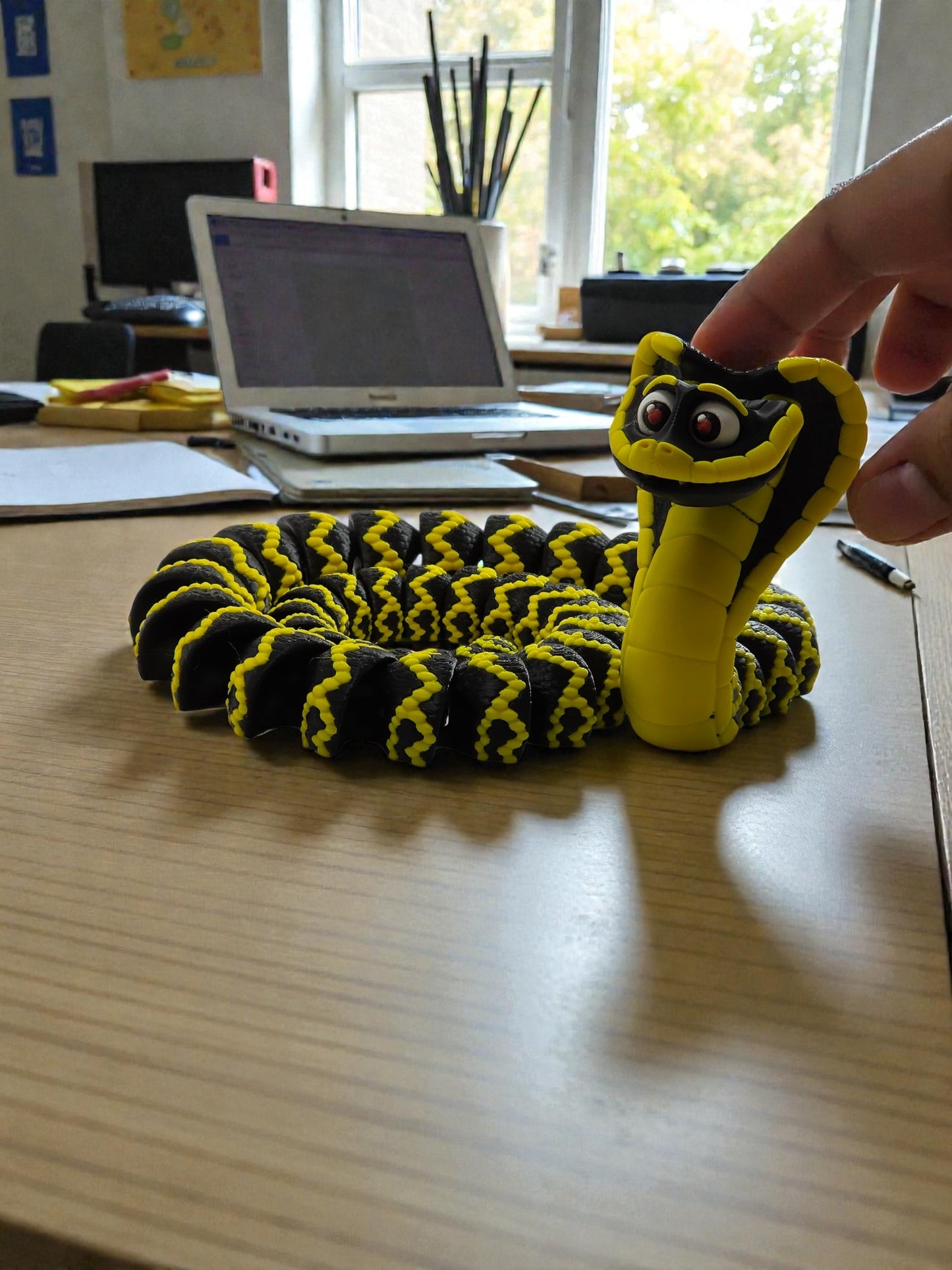 Yellow and black toy snake on a desk with a laptop and office supplies in the background