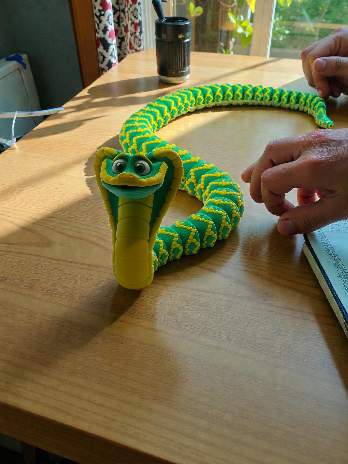 Green and yellow snake-shaped toy on a wooden table with a hand interacting with it.