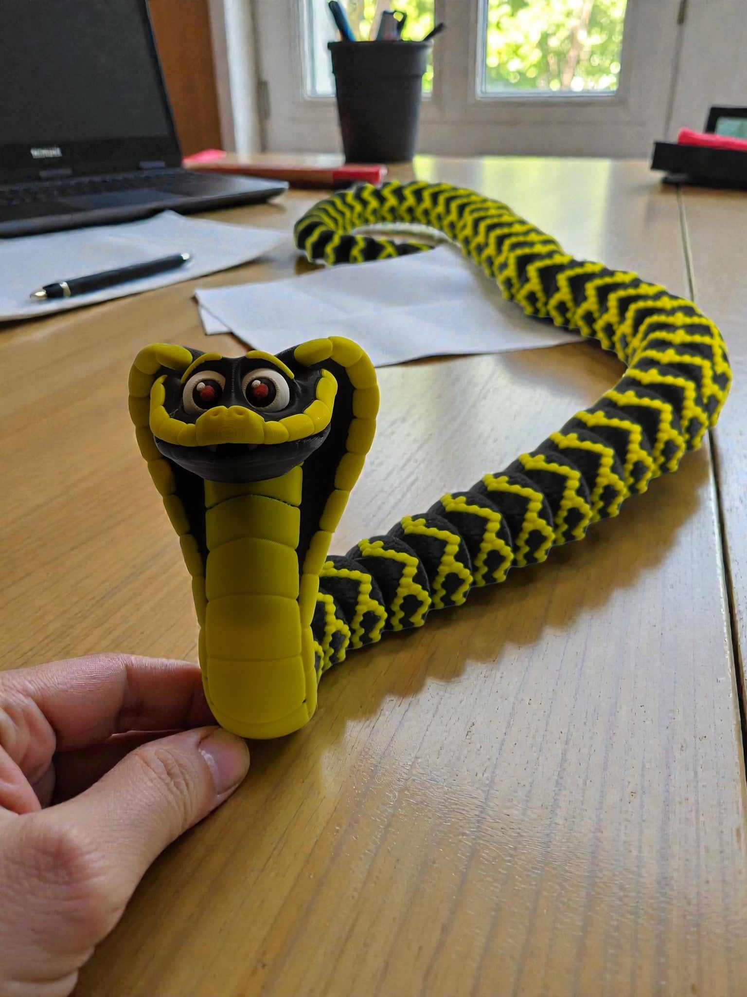 Yellow and black snake-on a wooden desk with office items in the background